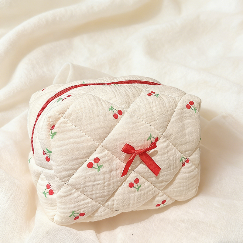 Cream quilted pouch with small red cherries, a red zipper, and a red ribbon bow on the front