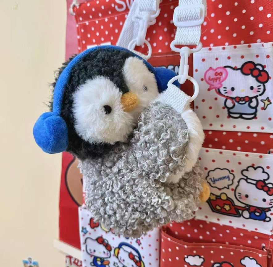 Fluffy grey penguin mini backpack with blue earmuffs worn over the shoulder with white straps