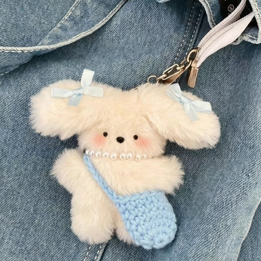 Cream plush bag charm with blue bows, pearl necklace, and a tiny crocheted blue bag attached to a metal clasp.