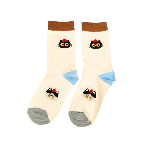 Cream crew socks with brown cuffs, blue heels, grey toes, and two black cat‑face designs with yellow eyes and red bows.