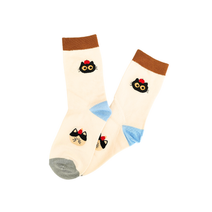 Cream crew socks with brown cuffs, blue heels, grey toes, and two black cat‑face designs with yellow eyes and red bows.