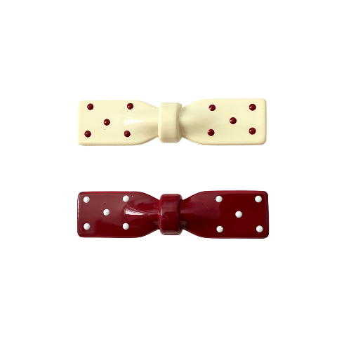 Two bow-shaped hair clips, one cream-colored with red polka dots and the other red with white polka dots, on a white background.