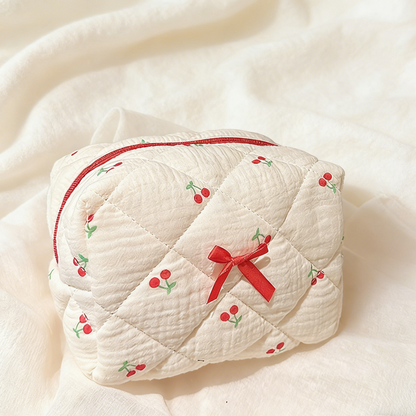 Cream quilted pouch with small red cherries, a red zipper, and a red ribbon bow on the front