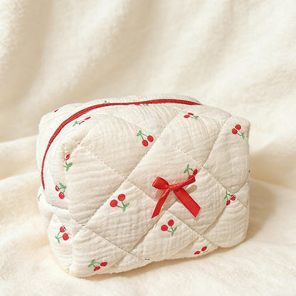 Cream quilted pouch with small red cherries, a red zipper, and a red ribbon bow on the front