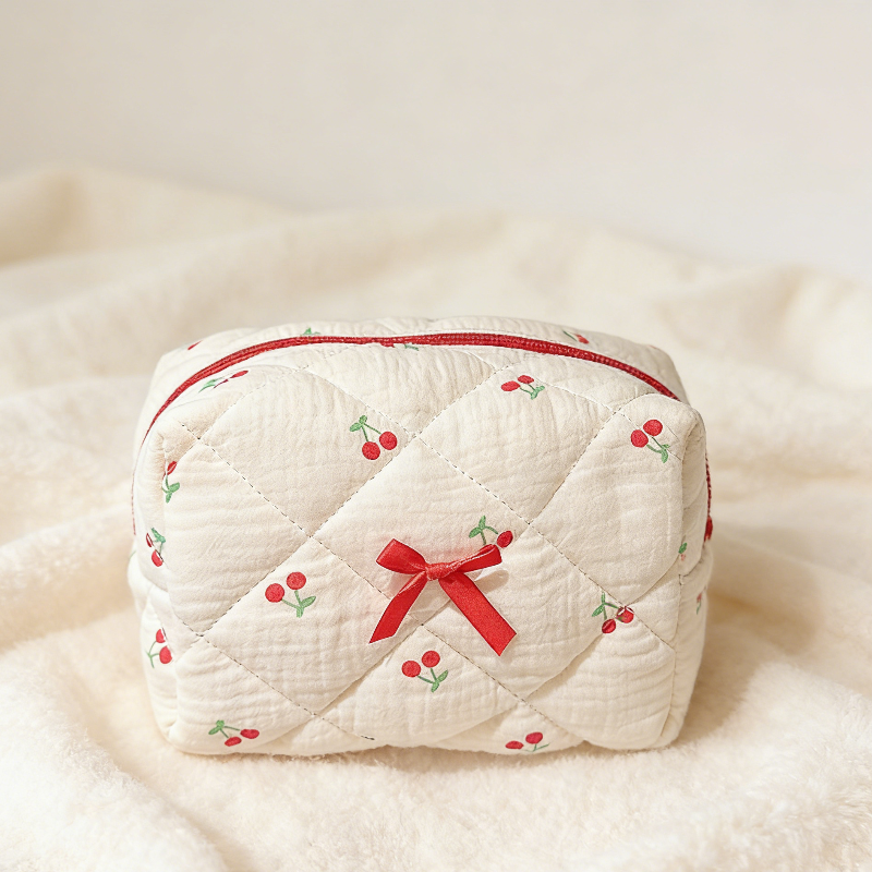 Cream quilted pouch with small red cherries, a red zipper, and a red ribbon bow on the front