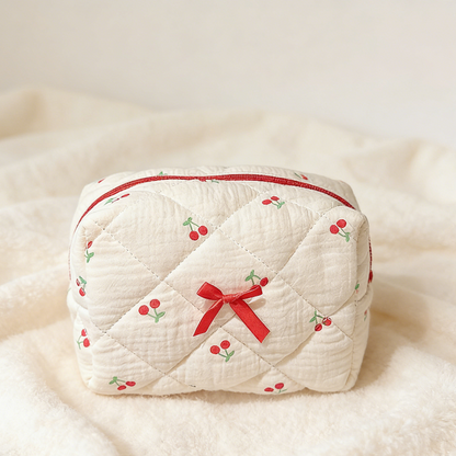 Cream quilted pouch with small red cherries, a red zipper, and a red ribbon bow on the front