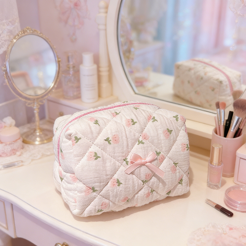 Cream quilted pouch with small rose motifs, a pink zipper, and a pink ribbon bow on the front.