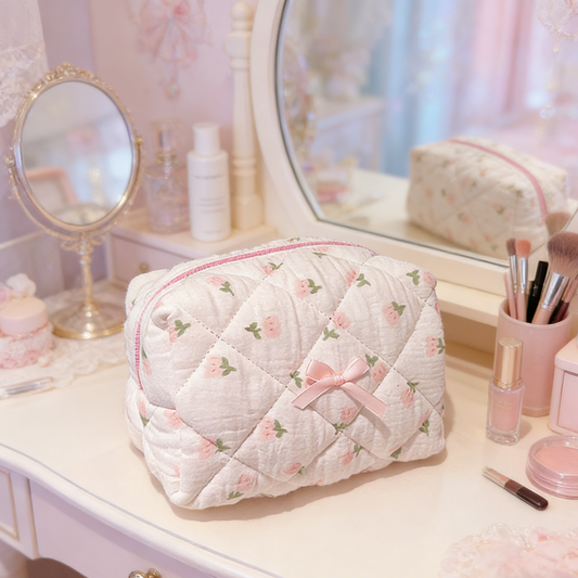 Cream quilted pouch with small rose motifs, a pink zipper, and a pink ribbon bow on the front.