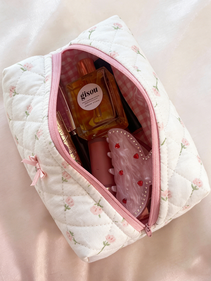 Cream quilted pouch with small rose motifs, a pink zipper, and a pink ribbon bow on the front.