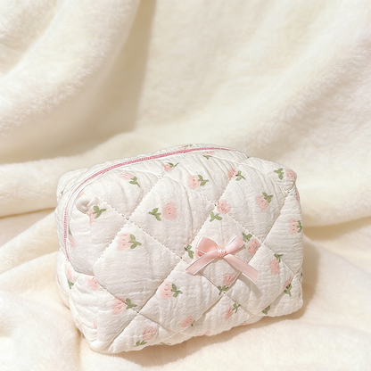 Cream quilted pouch with small rose motifs, a pink zipper, and a pink ribbon bow on the front.