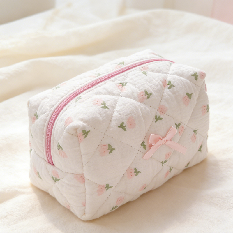 Cream quilted pouch with small rose motifs, a pink zipper, and a pink ribbon bow on the front.