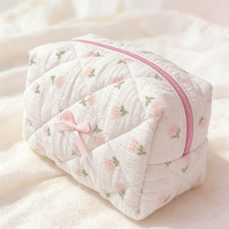 Cream quilted pouch with small rose motifs, a pink zipper, and a pink ribbon bow on the front.