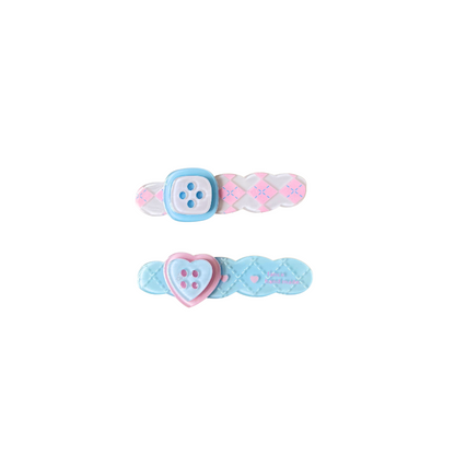 A sweet pastel hair clip duo featuring a pink criss‑cross clip with a button detail and a blue quilted clip with a heart button — perfect for soft‑girl, kawaii, and everyday cute hairstyles.