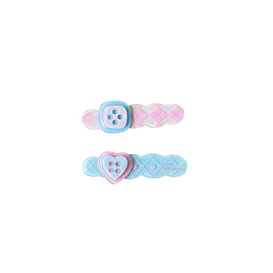A sweet pastel hair clip duo featuring a pink criss‑cross clip with a button detail and a blue quilted clip with a heart button — perfect for soft‑girl, kawaii, and everyday cute hairstyles.