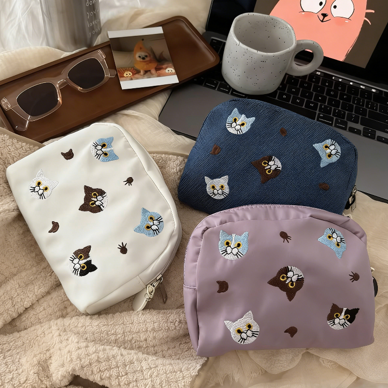 Three pouches in white, denim blue, and lavender, each with embroidered cat faces and paw prints