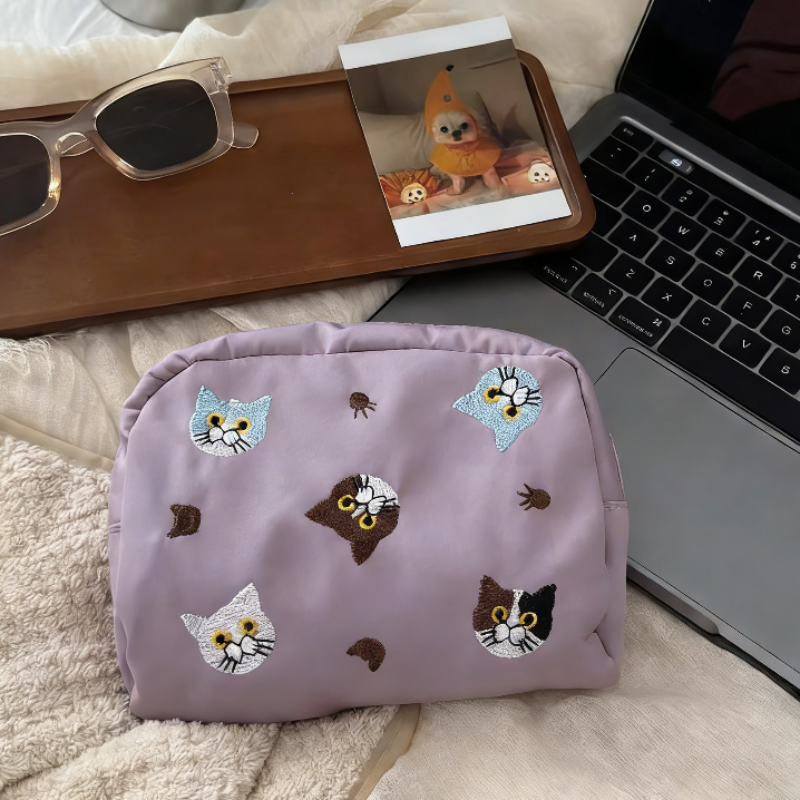 Three pouches in white, denim blue, and lavender, each with embroidered cat faces and paw prints