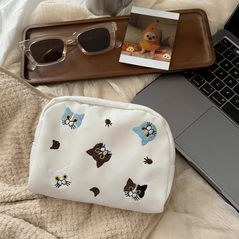 Three pouches in white, denim blue, and lavender, each with embroidered cat faces and paw prints