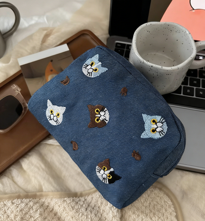 Three pouches in white, denim blue, and lavender, each with embroidered cat faces and paw prints