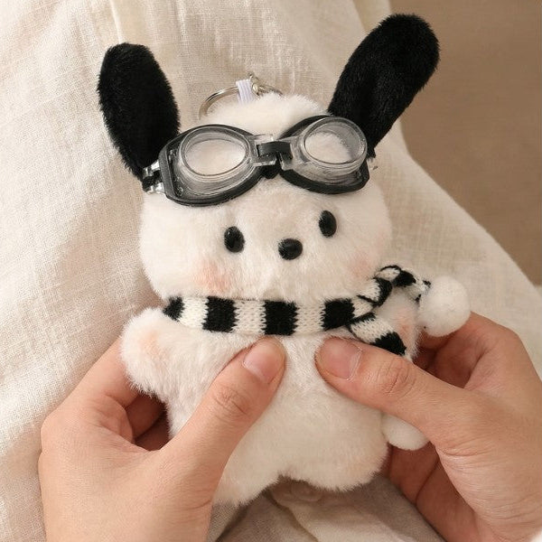 White plush dog bag charm with black ears, clear goggles, and a black‑and‑white striped scarf attached to a clip