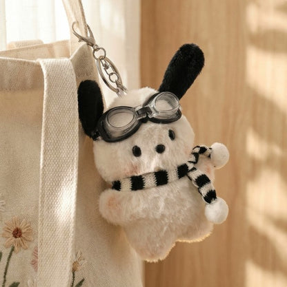 White plush dog bag charm with black ears, clear goggles, and a black‑and‑white striped scarf attached to a clip