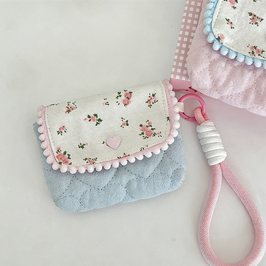 Floral-patterned pouch with pink pom-pom details and a pink strap on a light gray background