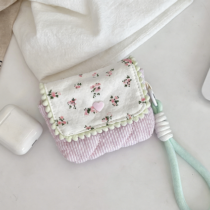 Four small quilted pouches in pastel colours, each with a patterned flap, pom‑pom trim, heart button, and matching wrist strap