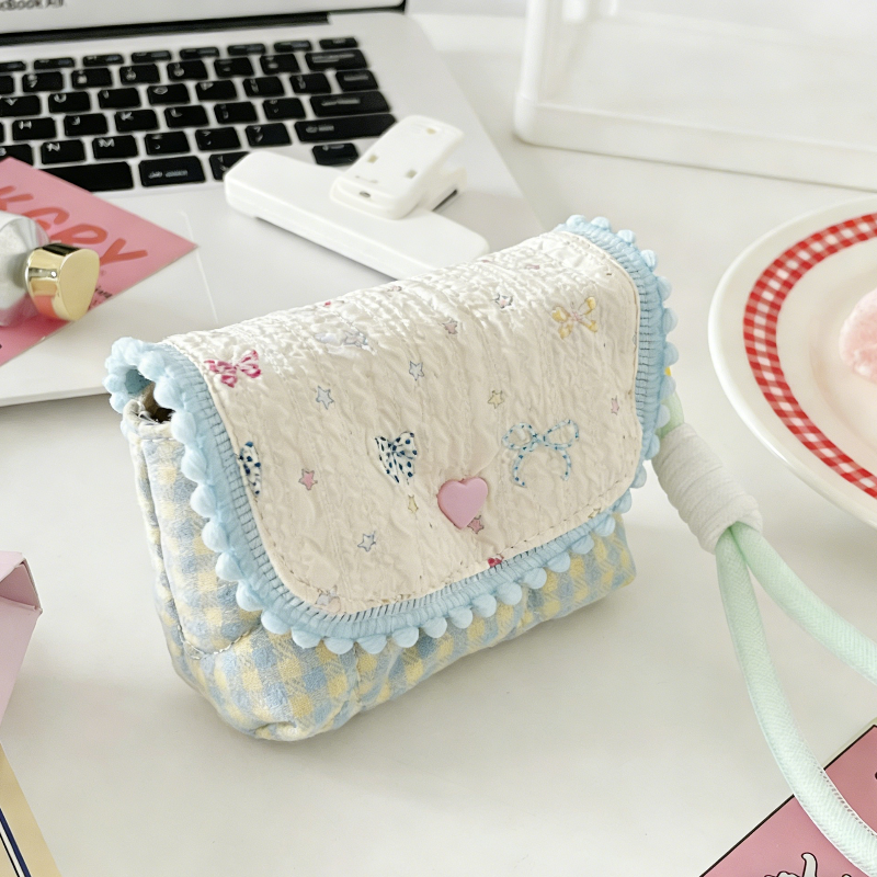 Four small quilted pouches in pastel colours, each with a patterned flap, pom‑pom trim, heart button, and matching wrist strap