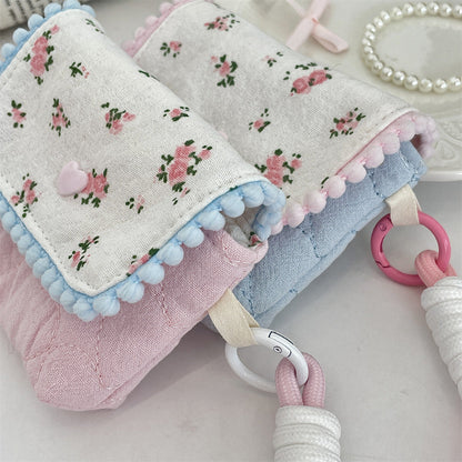 Four small quilted pouches in pastel colours, each with a patterned flap, pom‑pom trim, heart button, and matching wrist strap