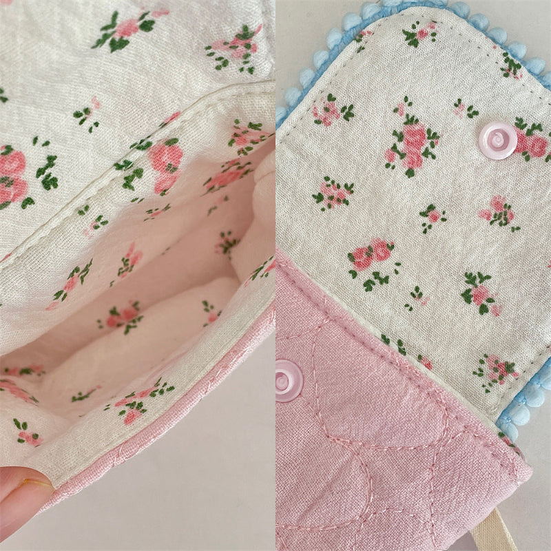 Four small quilted pouches in pastel colours, each with a patterned flap, pom‑pom trim, heart button, and matching wrist strap