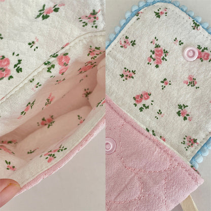 Four small quilted pouches in pastel colours, each with a patterned flap, pom‑pom trim, heart button, and matching wrist strap