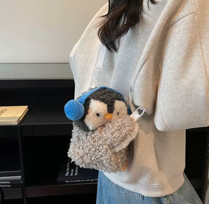 Fluffy grey penguin mini backpack with blue earmuffs worn over the shoulder with white straps