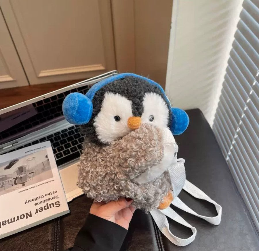 Fluffy grey penguin mini backpack with blue earmuffs worn over the shoulder with white straps