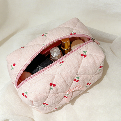 Pink quilted makeup bag with cherry embroidery on a white background
