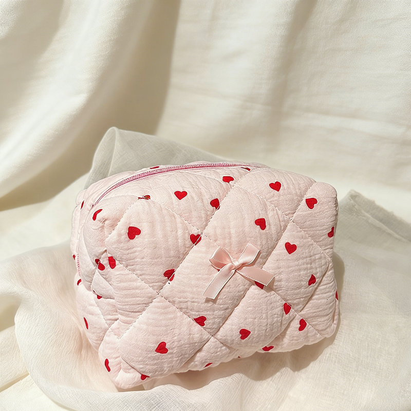 Pink quilted pouch with red heart patterns and a pink bow on a white fabric background