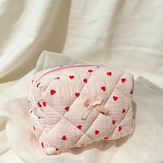 Pink quilted pouch with red heart patterns and a pink bow on a white fabric background