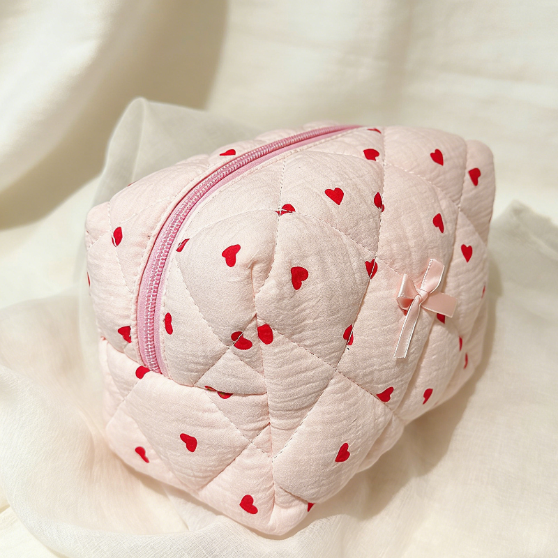 Pink quilted pouch with red heart patterns on a white background