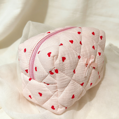 Pink quilted pouch with red heart patterns on a white background